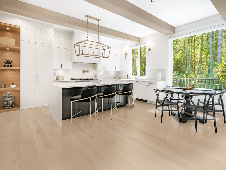 Bright, modern kitchen with white cabinets, a large island with black base and bar stools, pendant lighting, open shelving with decor, round dining table, and large windows overlooking a forested area.