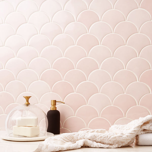 A bathroom counter with a white and gold soap dish, a black soap dispenser, a textured towel, and a pink scallop-patterned tile backsplash.