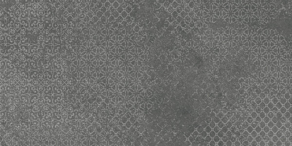 A dark gray, textured surface with faded geometric and floral patterns reminiscent of vintage style, similar to Shyft 24x48 Lace Deco tile. The subtle, partially worn designs create an aged, distressed appearance.