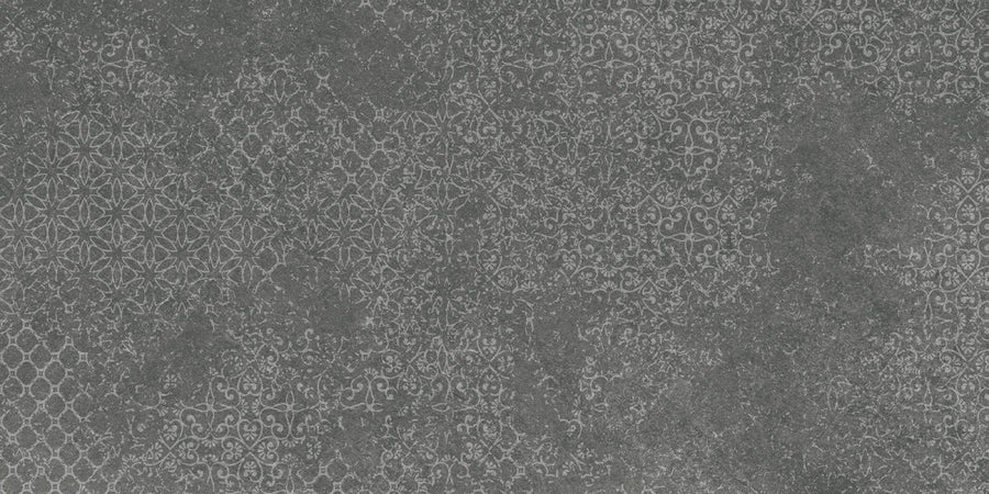 The Shyft 12x24 Lace Deco features a textured dark gray surface inspired by Brazilian slate, with repeating white lace-like patterns for a decorative, slightly distressed vintage tile look.