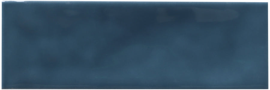 The Zephyr 2x6 Ceramic Tile is rectangular and glossy with a dark blue, slightly mottled surface and a reflective finish inspired by Mediterranean handcrafted luxury.
