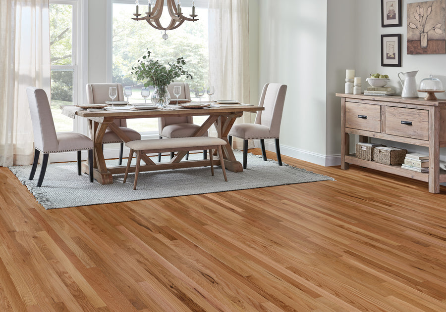 Bright dining room with light wood floors, a wooden table set for four, beige upholstered chairs, a bench, a sideboard with decor items, and large windows with sheer curtains letting in natural light.