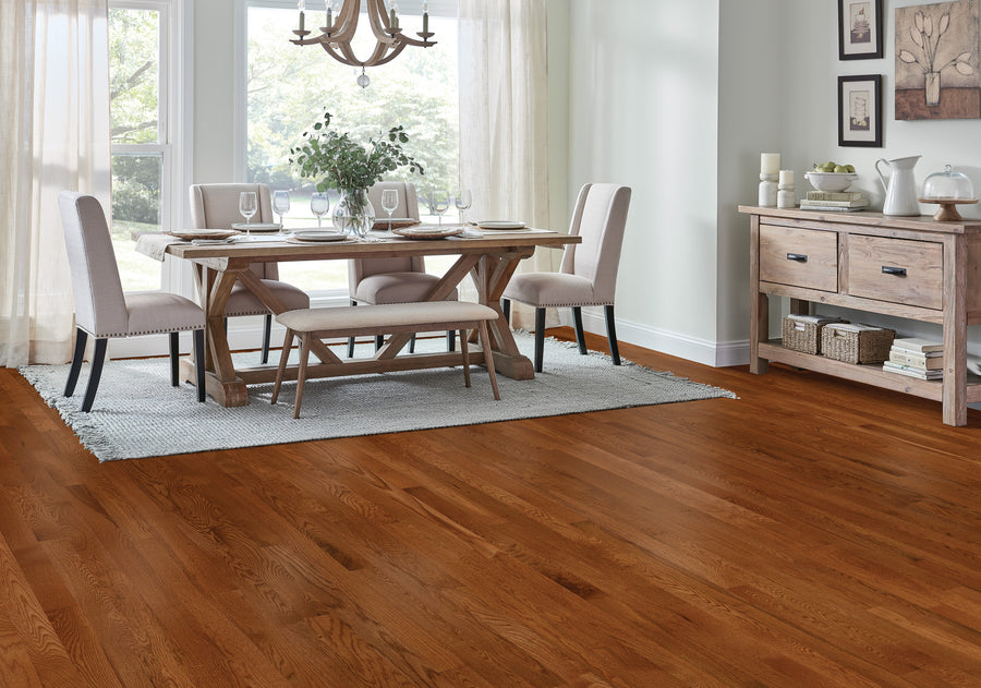 A bright dining room with hardwood floors, a wooden dining table set for four, a bench, chairs, a sideboard, and large windows with sheer curtains letting in natural light.