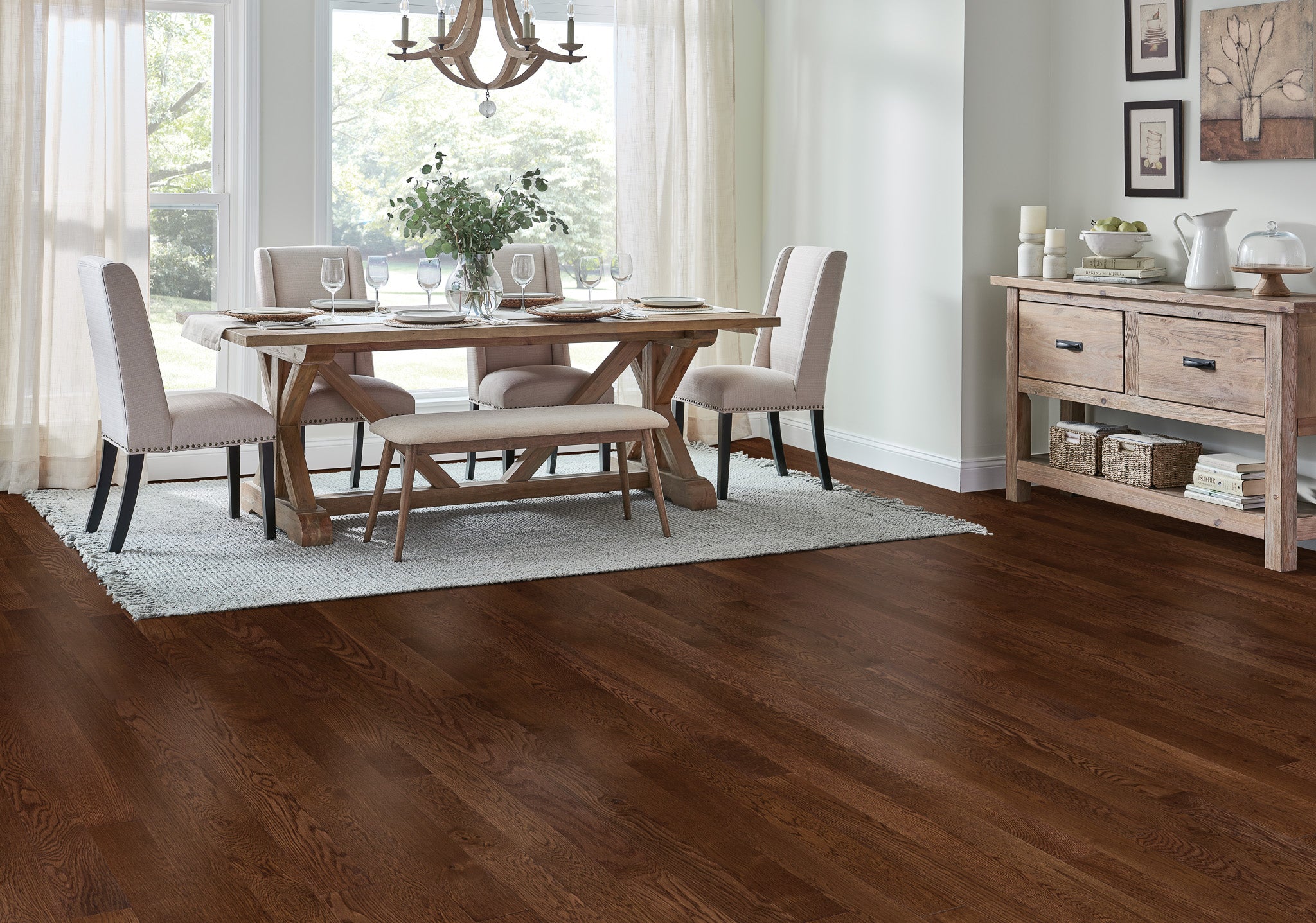 
		                            	A dining room with a wooden table, four cushioned chairs, a bench, and place settings. Large windows with sheer curtains let in natural light. Dark wood floors and a light rug complete the elegant, cozy space.
		                            