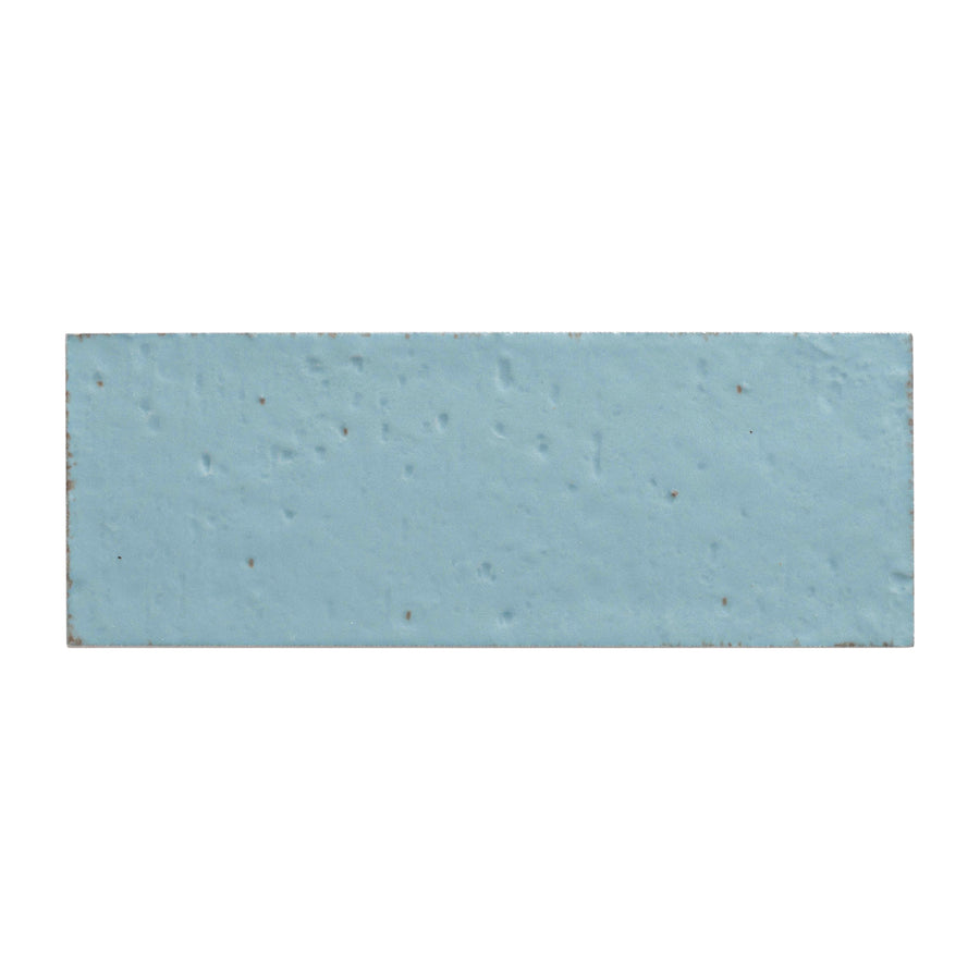 The Sarmento 3" x 8" Subway Porcelain Tile in Celdor features a rectangular, light blue elongated format with a slightly textured surface and subtle speckles.