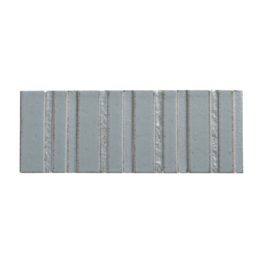 The Sarmento 3" x 8" Deco Subway Porcelain Tile in Jillene features a glossy light gray finish with vertical raised ridges and subtle edge color variations, creating a handcrafted look ideal for enhancing any space.