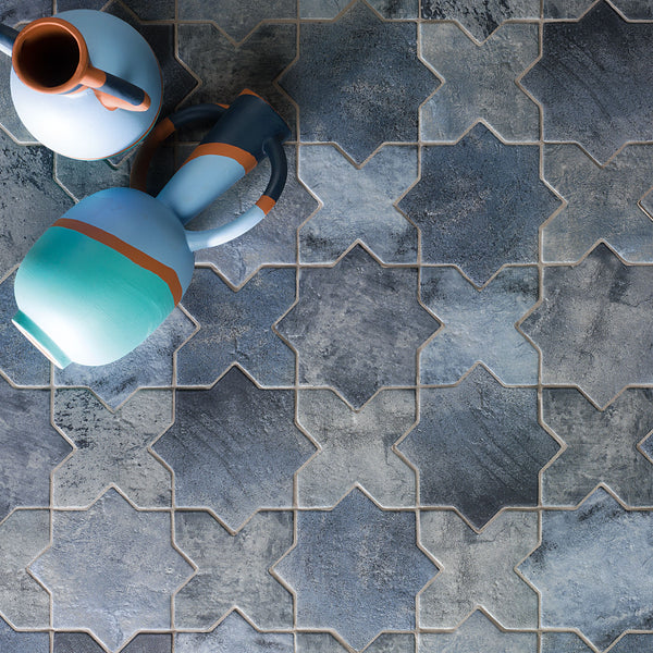 Blue and gray star-shaped tiles arranged in a pattern, with two ceramic vases featuring blue, teal, and orange bands placed on the tiles in the upper left corner of the image.