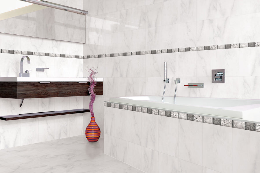 Modern bathroom with white marble walls and floor, a rectangular bathtub, a wall-mounted dark wood sink, a large mirror, and a colorful striped vase with decorative branches. Gray patterned tile accents line the walls.