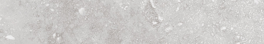 The Stream 4x24 Rectified Porcelain Tile features a gray and white textured surface with subtle speckles, natural veining, and irregular patches, creating an authentic travertine-look stone enhanced by slight roughness.