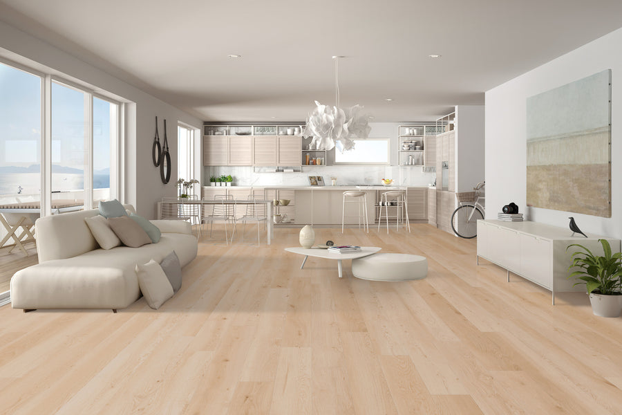 Spacious modern living room and kitchen with light wood floors, white furniture, large windows, abstract wall art, and a plant. Natural light fills the open-plan space, creating a bright and airy atmosphere.