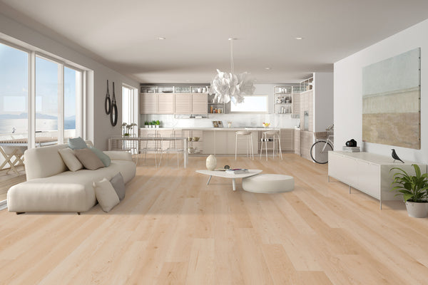 Spacious modern living room and kitchen with light wood floors, white furniture, large windows, abstract wall art, and a plant. Natural light fills the open-plan space, creating a bright and airy atmosphere.