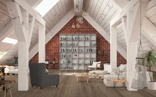 A cozy attic living space with slanted white wooden ceilings, exposed beams, a large bookshelf against a red brick wall, assorted modern furniture, and plants on a wooden floor.