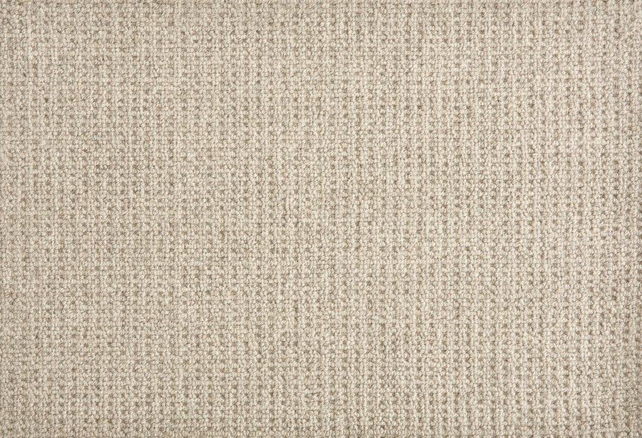 A close-up of Martina Berber Carpet in Shadow shows its beige, textured surface with a subtle woven pattern and grid-like threads—perfect for contemporary spaces needing soft, durable flooring for high-traffic areas. The surface is soft and slightly raised.