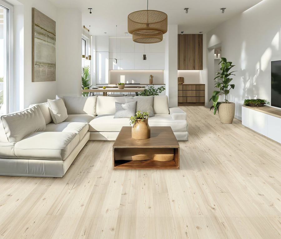 Modern living room featuring Glacial Isle 8 11/32" Waterproof Laminate light wood flooring, a white sectional sofa, wooden coffee table, large windows, potted plants, and an open kitchen with white cabinets and wicker light fixtures.