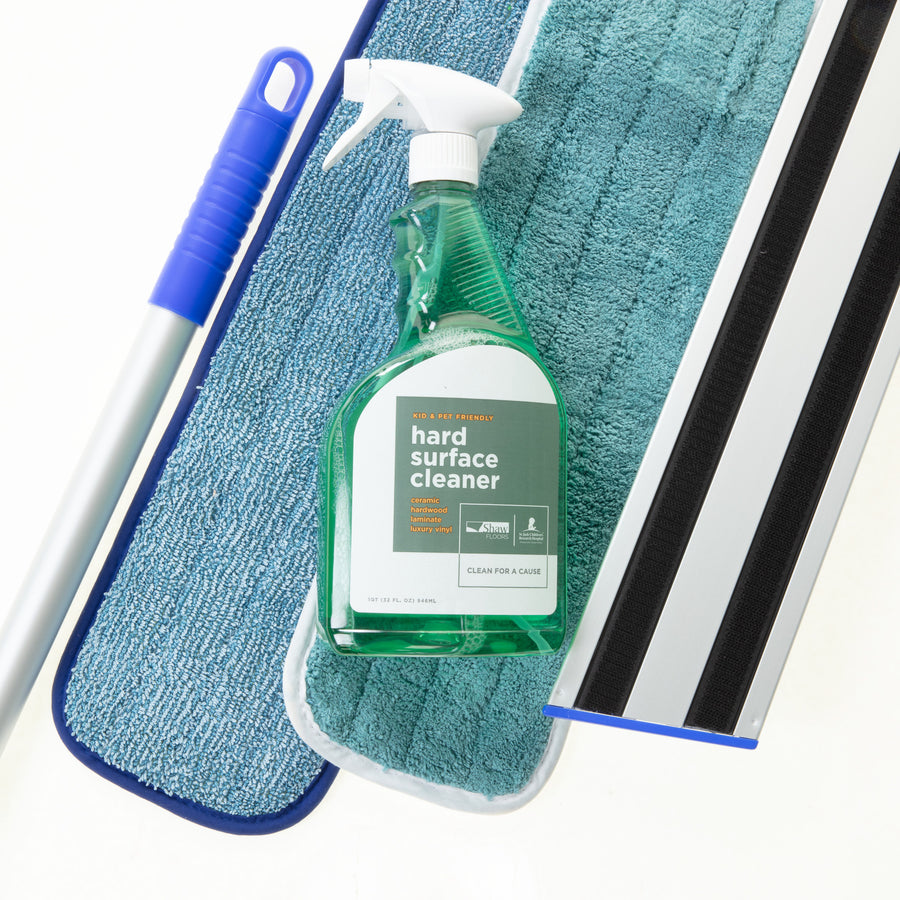 The Shaw Hard Surface Cleaning Kit, featuring a bottle of floor cleaner on a blue microfiber mop pad with the mop handle and head visible, is ideal for maintaining hard surface floors.