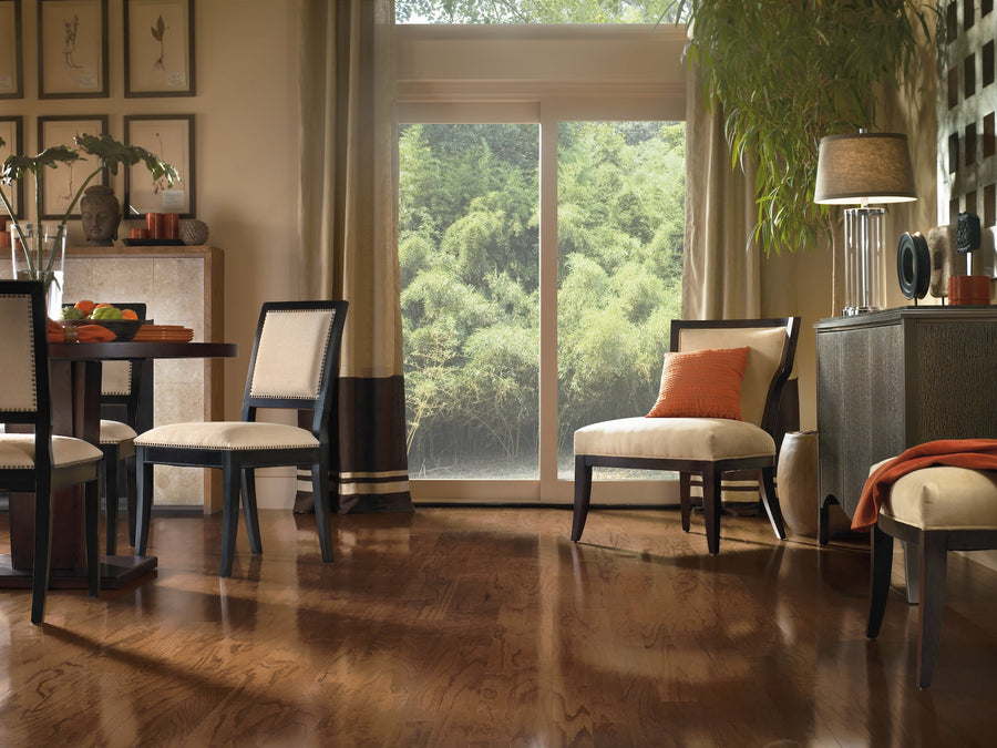 A modern dining room with wooden floors, neutral-toned chairs, a dining table, a sliding glass door with a view of greenery, and decorative accents including plants, cushions, and wall art.