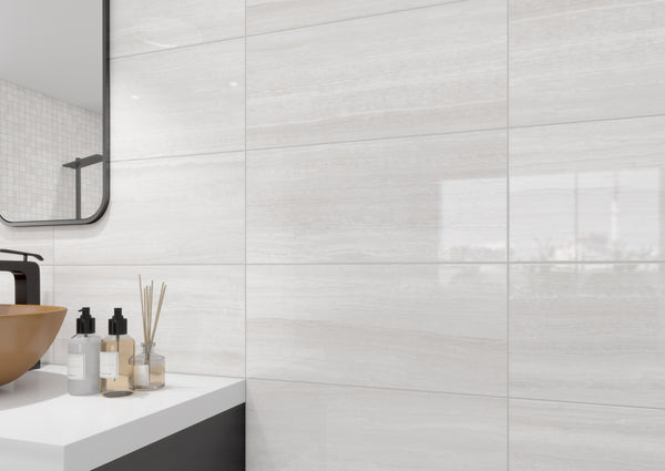 Modern bathroom with glossy white and beige marble-look tiles, a rectangular mirror, a brown vessel sink, and bottles and a reed diffuser on a white countertop.