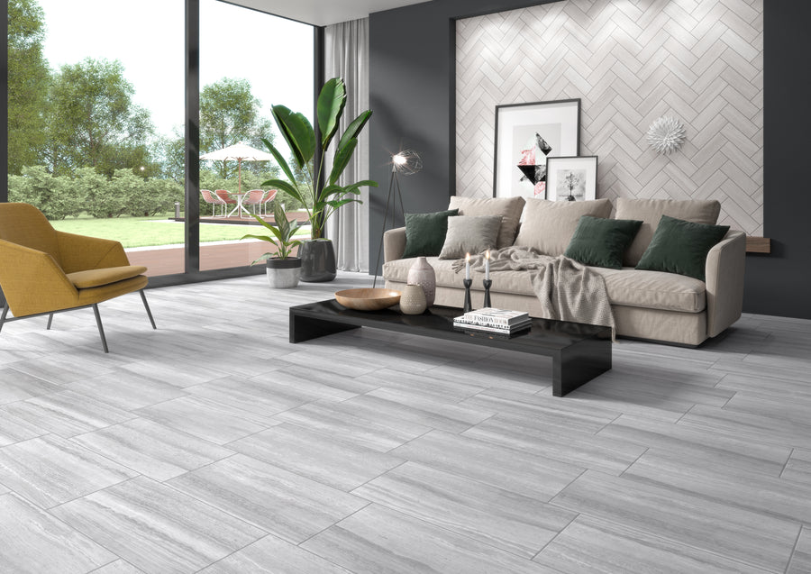 Modern living room with large windows, a beige sofa with green pillows, a yellow chair, a low black coffee table, potted plants, and light gray floor tiles. Outdoor patio and greenery visible through the windows.