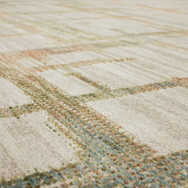 Close-up view of a textured carpet with a geometric pattern in muted tones of beige, green, blue, and orange. The image highlights the soft fibers and subtle color variations.