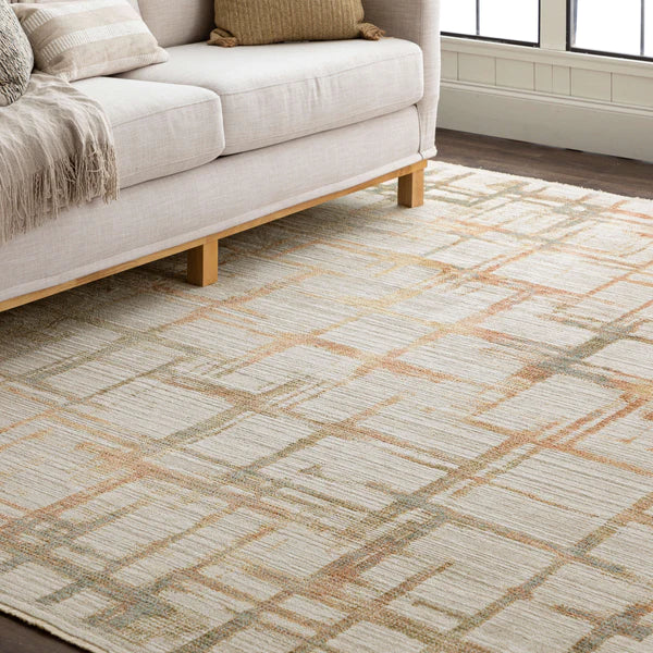 A beige and cream area rug with a subtle plaid pattern lies on a wooden floor next to a light-colored sofa with tan cushions and a throw, near a large window with white trim.