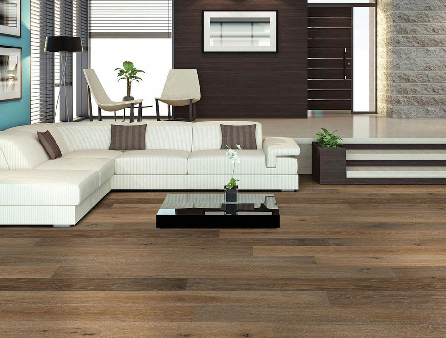 Modern living room with a white sectional sofa, brown and beige cushions, a black coffee table with a plant, wooden flooring, and large windows letting in natural light. Stairs lead to a split-level area with chairs and more plants.