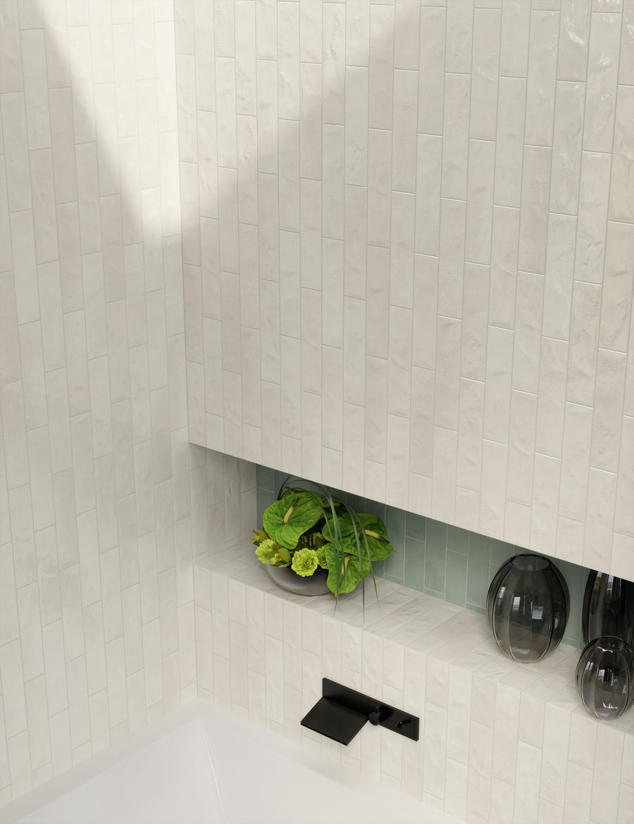 A modern bathroom with glossy, vertical cream-colored tiles, a black wall-mounted faucet, a built-in shelf holding a bowl of green plants, and two dark decorative vases.
