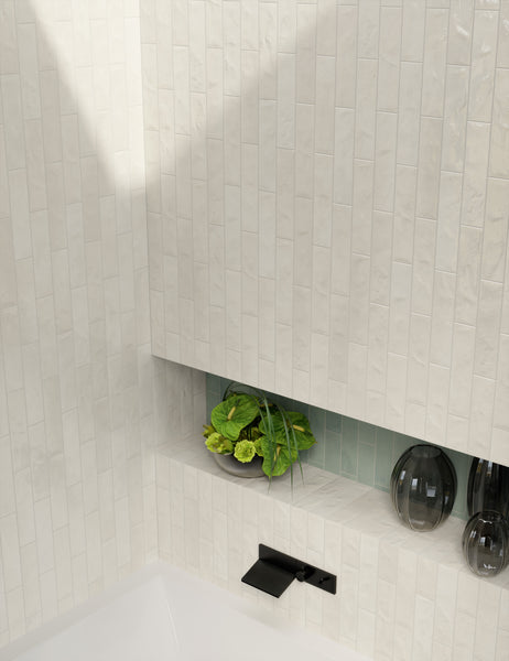 A modern bathroom with glossy, vertical cream-colored tiles, a black wall-mounted faucet, a built-in shelf holding a bowl of green plants, and two dark decorative vases.