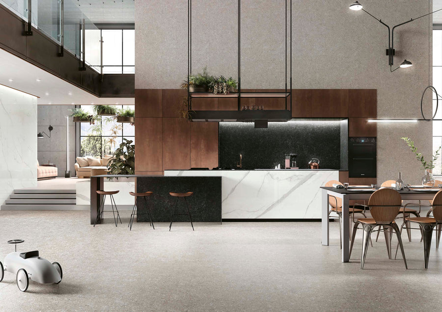 Modern open-plan kitchen and dining area with minimalist decor, featuring a marble island, wooden cabinets, high ceilings, hanging lights, indoor plants, and a small toy car on the floor. Living room visible in the background.