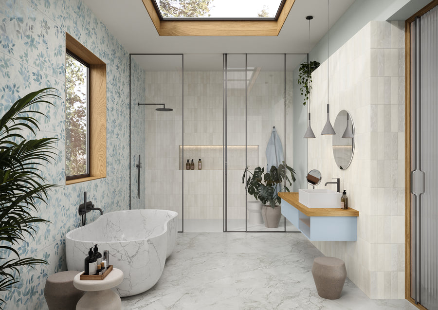 Modern bathroom with a marble bathtub, walk-in glass shower, floating vanity with round mirror, skylight, potted plants, blue floral wallpaper, and a large window providing natural light.