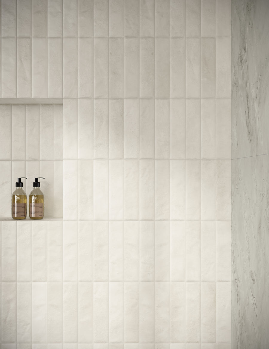 A bathroom wall with vertical rectangular beige tiles, a recessed shelf, and two pump bottles of soap or lotion placed inside the shelf. The overall appearance is clean and minimalistic.