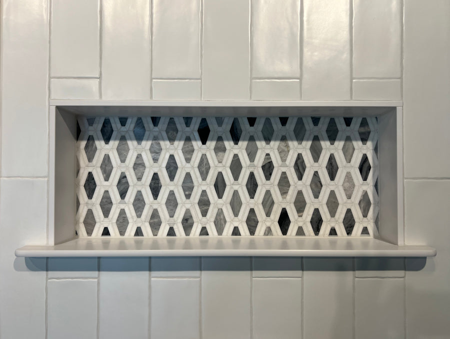 A recessed shower shelf with a white hexagonal tile pattern on the back wall, surrounded by large rectangular white tiles.