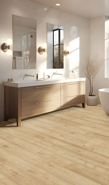 A modern bathroom with light wood flooring, a double-sink vanity with wood drawers, two wall mirrors, sconce lights, a large window, a white freestanding tub, and a decorative branch arrangement in a vase.