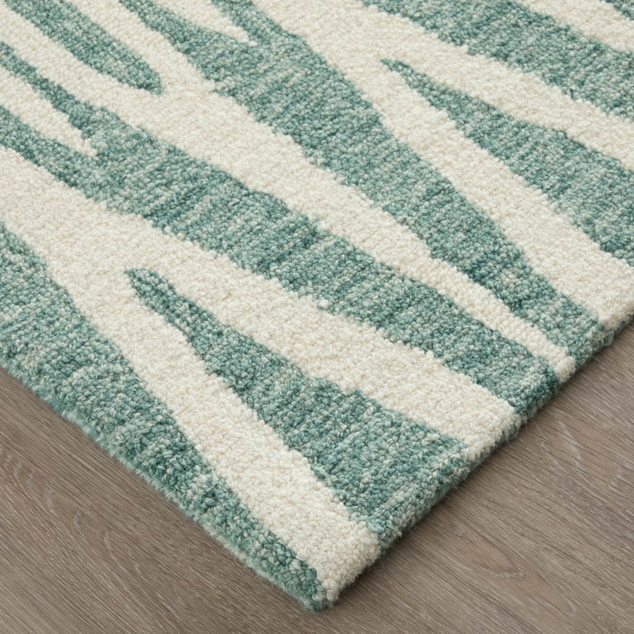 A close-up of a rectangular rug with a textured, raised pattern of irregular light green and cream stripes, placed on a light wood floor.
