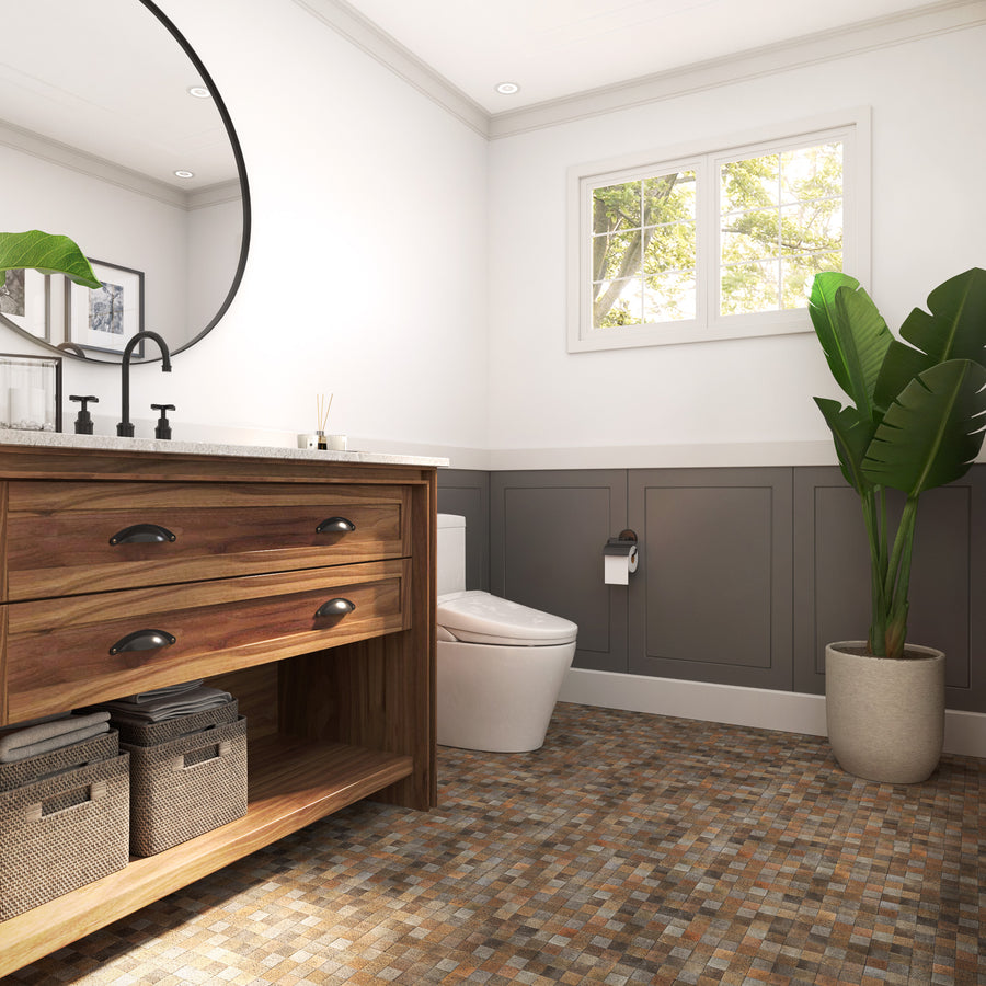 A modern bathroom with a wooden vanity, round mirror, mosaic tile floor, toilet, potted plant, and a window letting in natural light. Gray wainscoting and neutral tones create a clean, cozy feel.