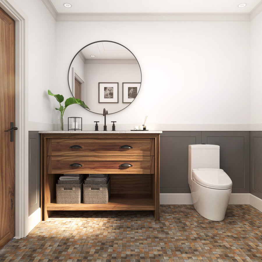 Modern bathroom with a wood vanity, two baskets underneath, a round mirror above, a white toilet, mosaic tile floor, and gray wainscoting on white walls. Two framed photos and a green plant decorate the space.