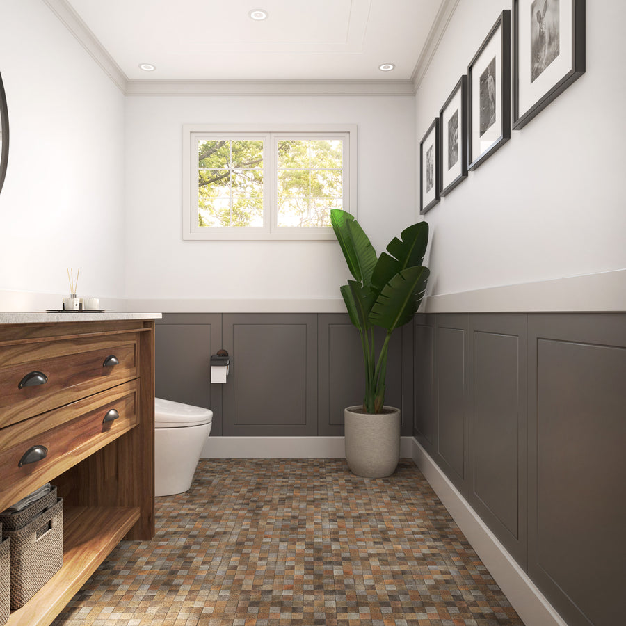 A modern bathroom features gray wainscoting, a wooden vanity, mosaic tile flooring, a potted green plant, framed black-and-white photos on the wall, a toilet, and a window letting in natural light.