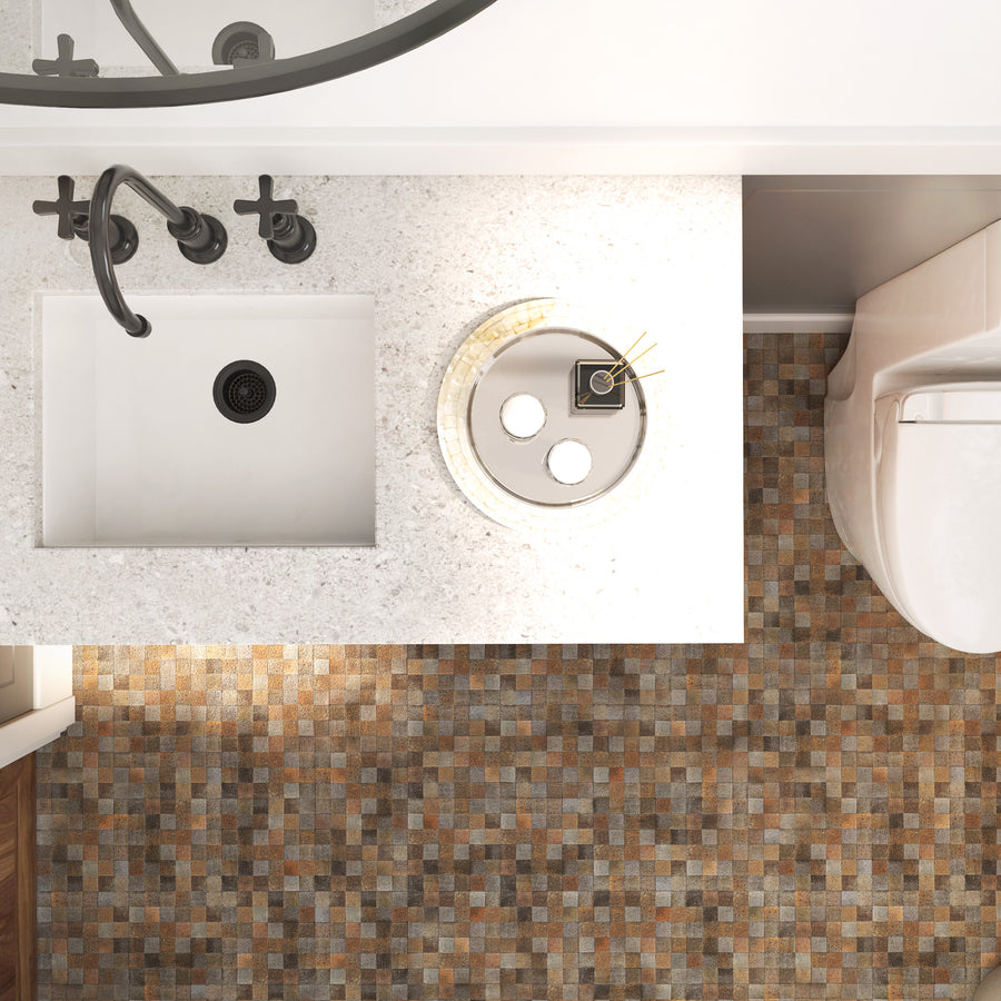 A top-down view of a bathroom with a white sink, black fixtures, a round tray holding small jars and sticks, and a toilet. The floor has a mosaic tile pattern in brown and beige tones.