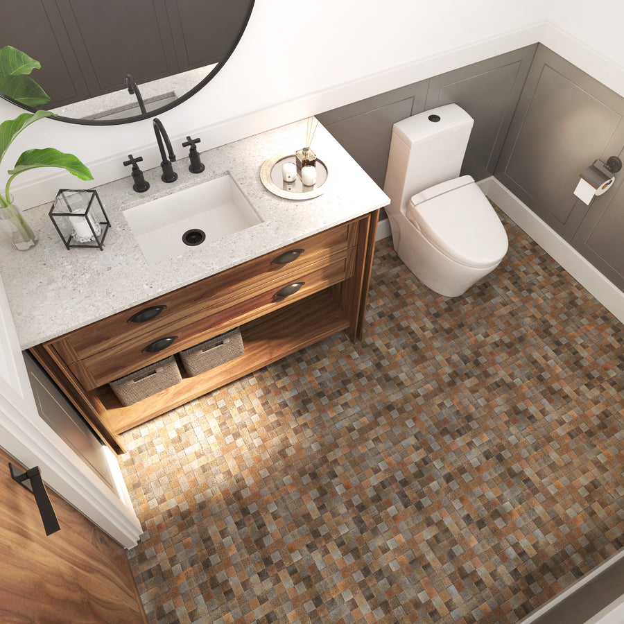 Modern bathroom with a wood vanity, white sink, round mirror, potted plant, toilet, and mosaic tile floor in brown and beige tones. Baskets are stored under the sink.
