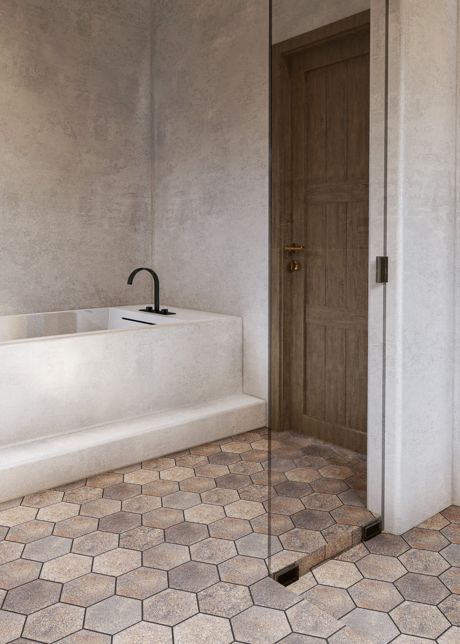 Minimalist bathroom with a built-in white bathtub, matte black faucet, wooden door, and hexagonal beige floor tiles. A partial glass shower screen is visible on the right side.