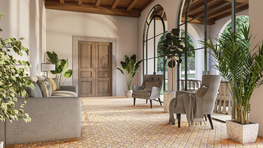A sunlit room with large arched windows, gray sofa and chairs, potted plants, and a wooden ceiling. Natural light fills the space, highlighting the tiled floor and cozy, inviting seating area.