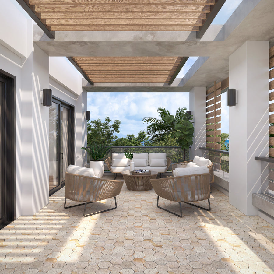 Modern outdoor patio with light tile flooring, wooden pergola, and contemporary furniture including a white sofa, round table, and four wicker chairs. Potted plants and greenery surround the seating area; sky visible above.
