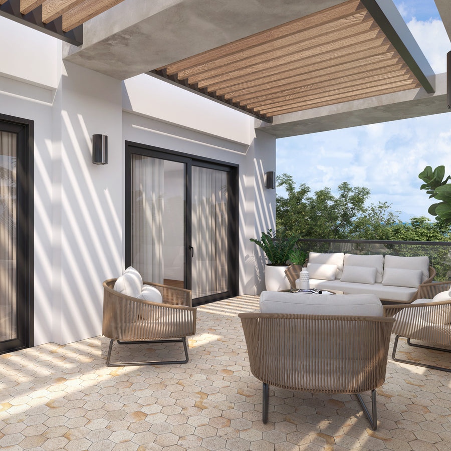 Modern outdoor patio with beige cushioned chairs and a sofa, hexagonal tile flooring, a pergola with wood slats casting shadows, and potted plants, set against a backdrop of trees and blue sky.