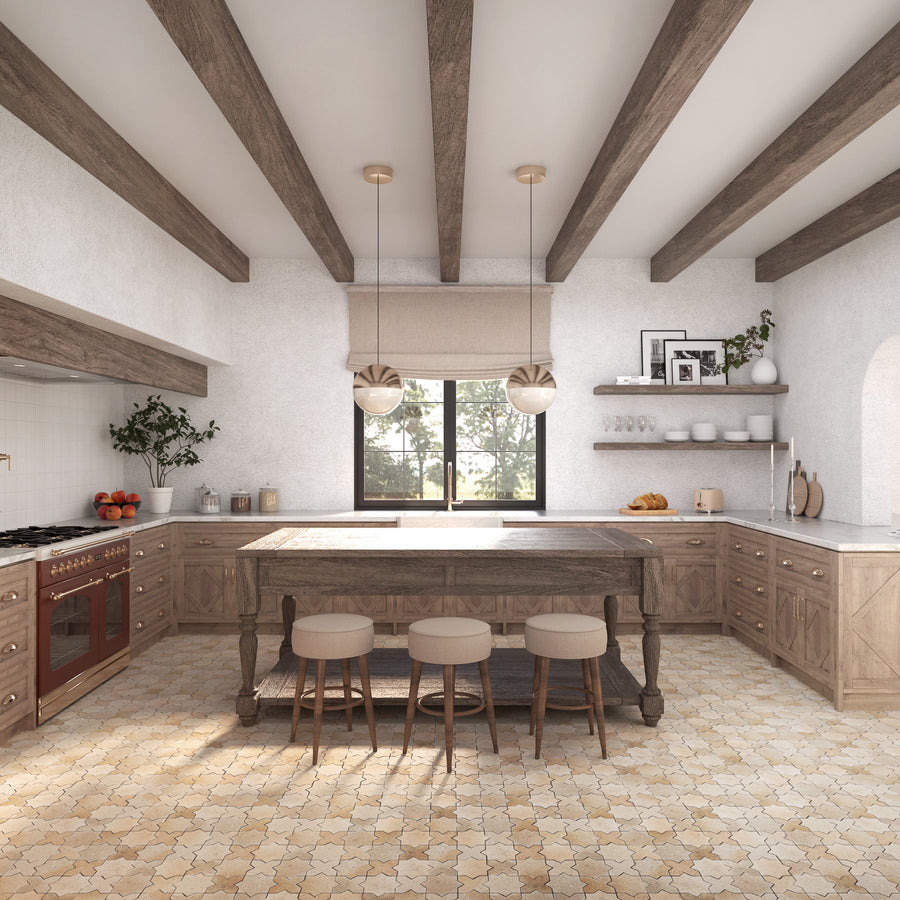 Bright, rustic kitchen with wooden beams, a large island with three stools, light wood cabinets, a red oven, open shelves with dishes, and a window letting in natural light. Warm neutral tones throughout.
