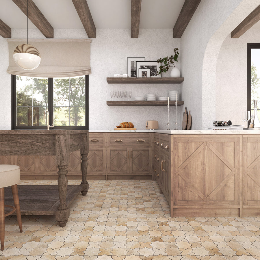 Bright rustic kitchen with wooden cabinets, open shelves holding decor and dishes, a window with beige Roman shade, patterned tile floor, exposed ceiling beams, and a kitchen island with a round stool.