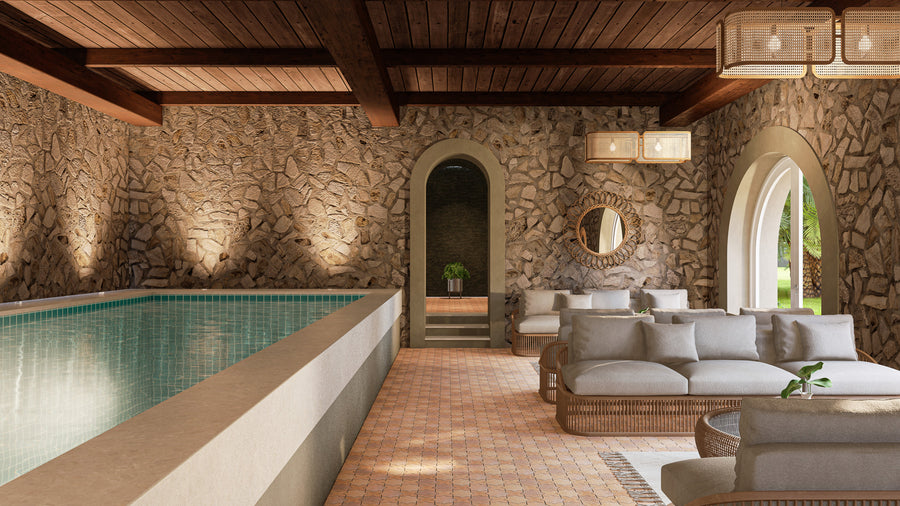 Indoor pool area with stone walls, wooden ceiling beams, arched doorways, and large windows. Cozy seating with light cushions and a round mirror enhance the warm, inviting atmosphere. Soft lighting adds to the tranquil space.