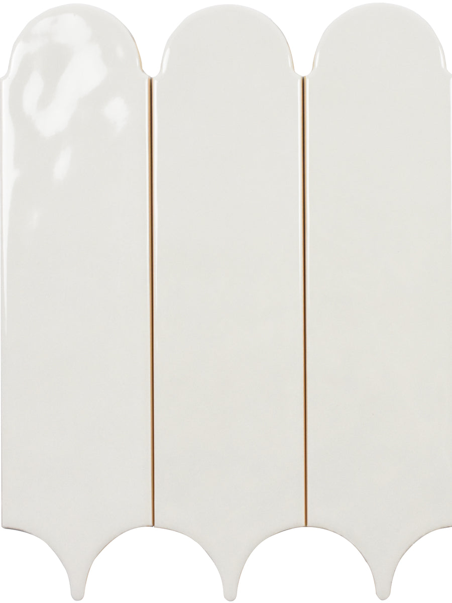 Three Tranquill 3x12 Glazed Ceramic Tiles, featuring a glossy off-white finish, are placed side by side. Each has a rounded top and scalloped bottom, forming an arched, decorative pattern with timeless appeal.