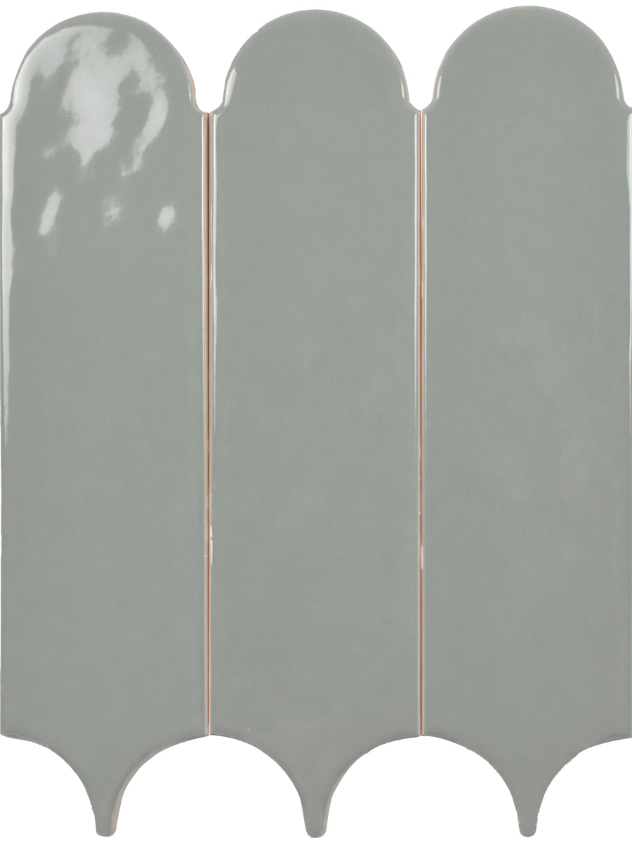 Three vertical Tranquill 3x12 Glazed Ceramic Tiles in glossy light gray, with rounded tops and pointed bottoms, are arranged side by side in a repeating scalloped pattern for a timeless neutral look.