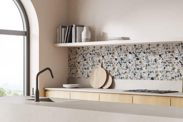 Minimalist kitchen with light wood cabinets, a terrazzo tile backsplash, a black faucet, and a large arched window. Open shelves display books, dishes, decor, and round wooden cutting boards on the counter.