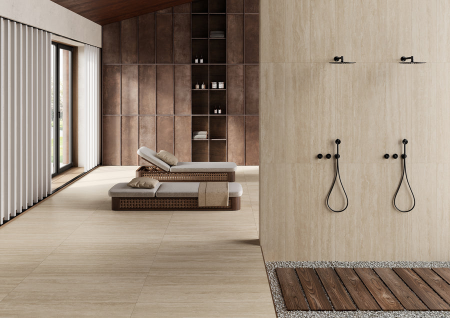 A modern spa room with two loungers, wooden shelving along the back wall, and a double shower area with black fixtures and a wooden slatted floor. Light streams in through large windows with vertical blinds.