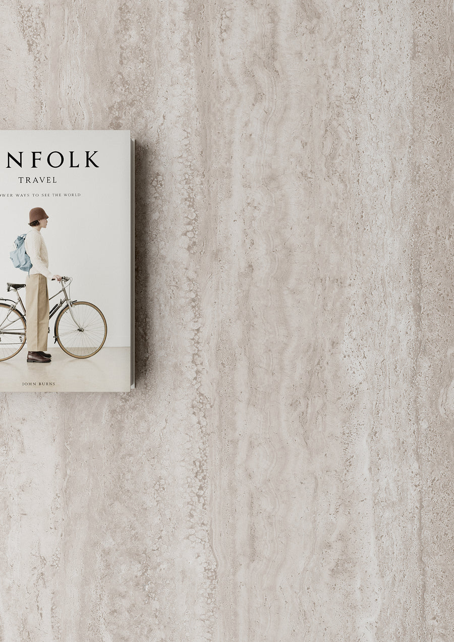 A book titled Kinfolk Travel with a cover image of a person standing beside a bicycle, placed on a light beige textured surface with ample empty space to the right.